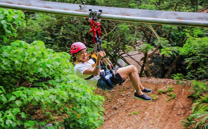 Tourist ziplining at Hanuman World amidst lush greenery.