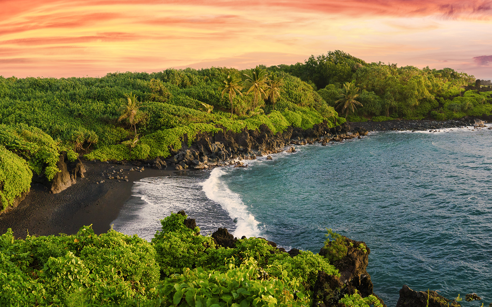Black sand beach with lush greenery along the Road to Hana, Hawaii.
