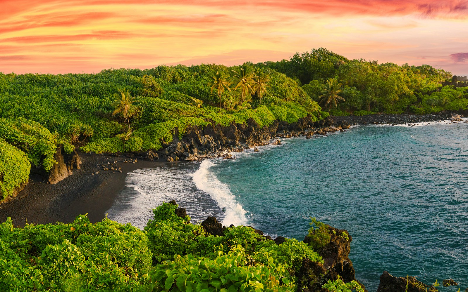 Black sand beach with lush greenery along the Road to Hana, Hawaii.