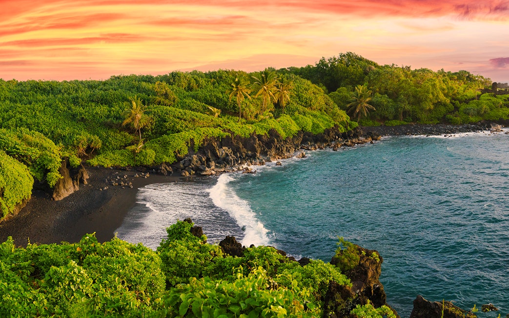 Black sand beach with lush greenery along the Road to Hana, Hawaii.