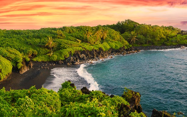 Black sand beach with lush greenery along the Road to Hana, Hawaii.