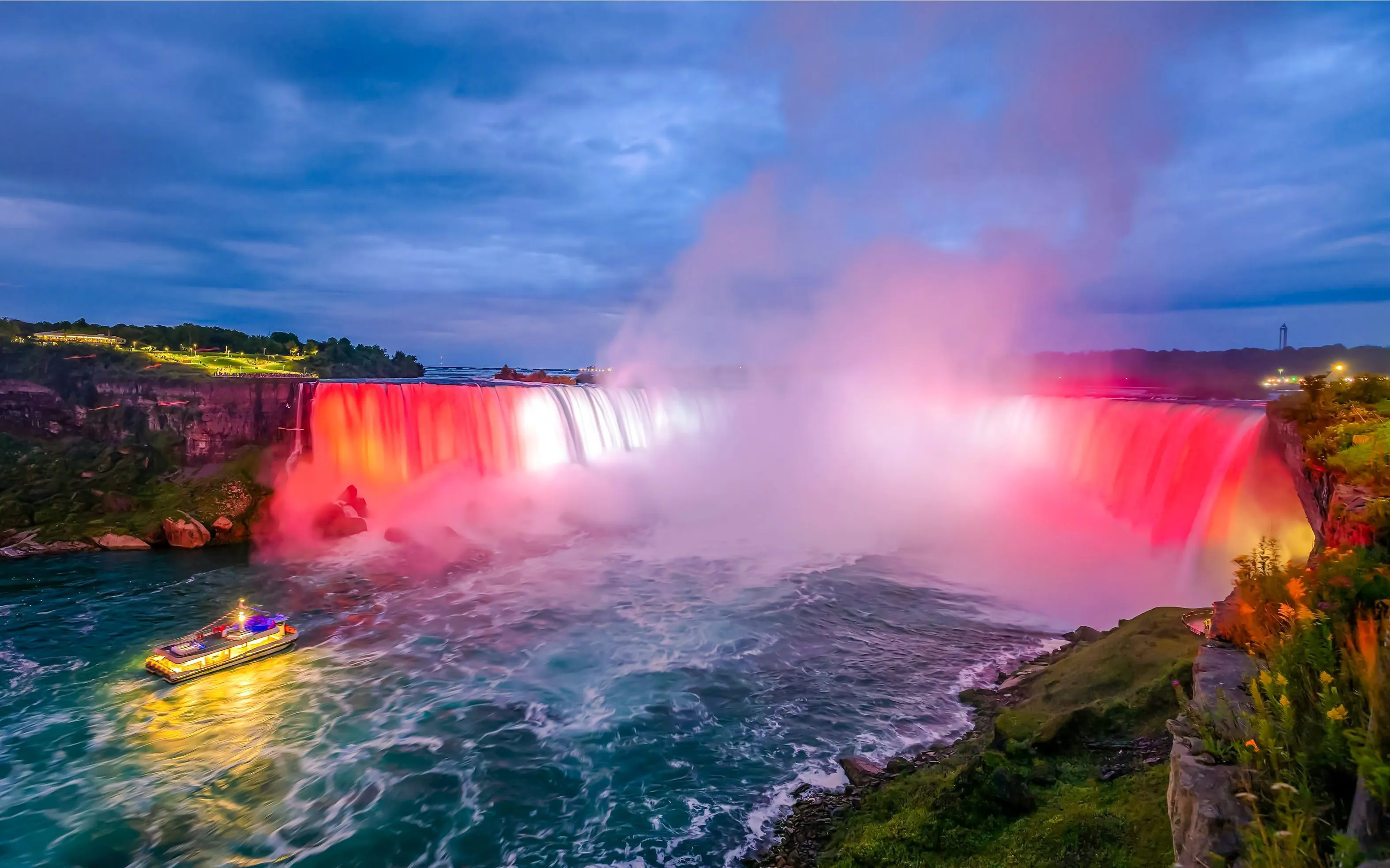 Niagara Falls illuminated at night with a boat on the water, view from Ontario, Canada.