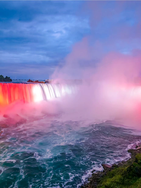 Niagara Falls illuminated at night with a boat on the water, view from Ontario, Canada.