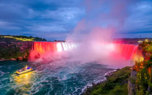 Niagara Falls illuminated at night with a boat on the water, view from Ontario, Canada.