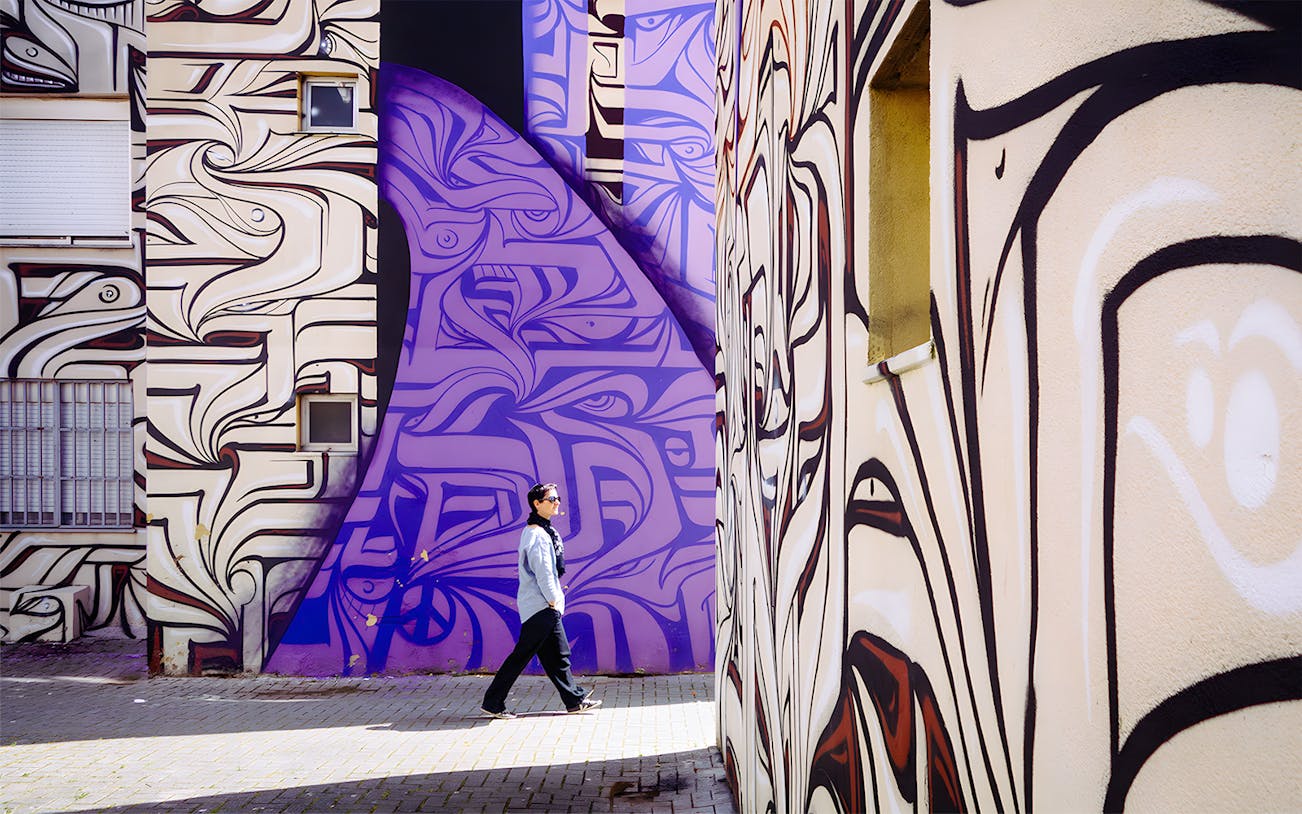 Person walking past vibrant street art murals in Lisbon.