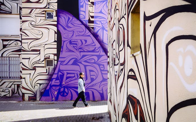 Person walking past vibrant street art murals in Lisbon.