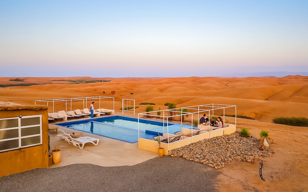 Poolside lounge area at Agafay Desert camp near Marrakech with desert landscape in the background.