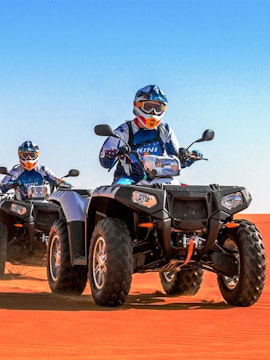 Quad biking on red sand dunes during a desert safari in Dubai.