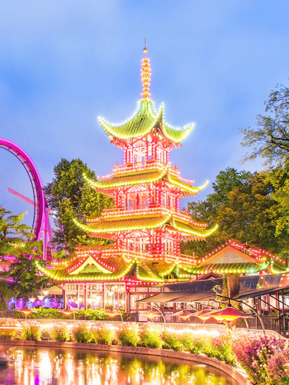 Tivoli Gardens pagoda illuminated at night with nearby rides, Copenhagen.