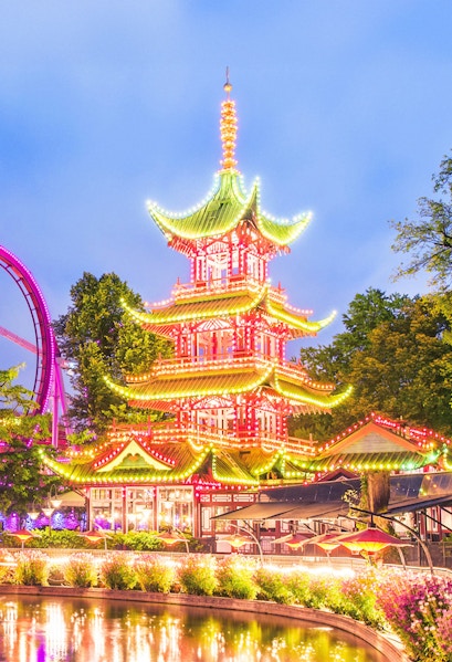 Tivoli Gardens pagoda illuminated at night with nearby rides, Copenhagen.