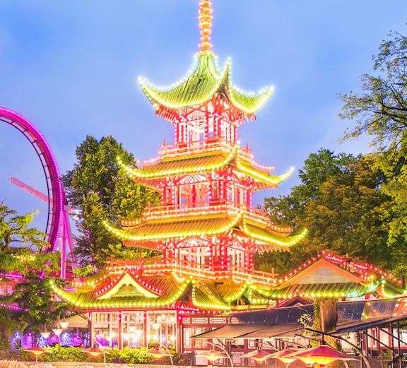 Tivoli Gardens pagoda illuminated at night with nearby rides, Copenhagen.