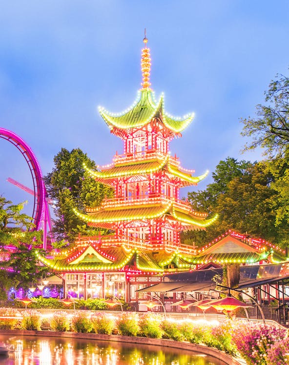 Tivoli Gardens pagoda illuminated at night with nearby rides, Copenhagen.