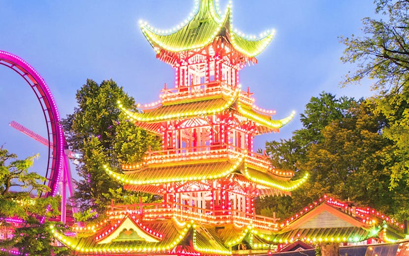 Tivoli Gardens pagoda illuminated at night with nearby rides, Copenhagen.