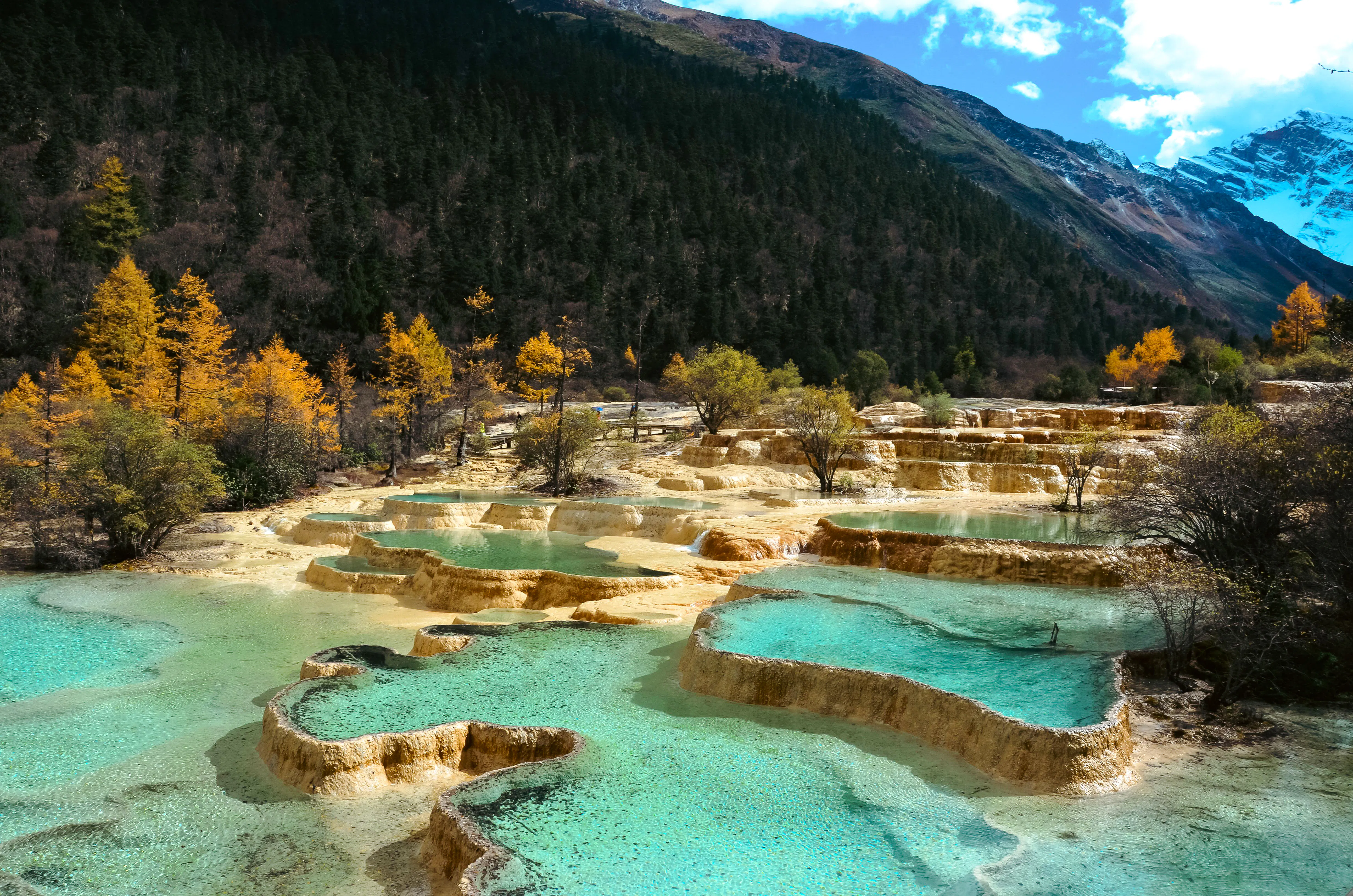 Terraced turquoise pools at Huanglong National Park, Chengdu, with forested mountains in the background.