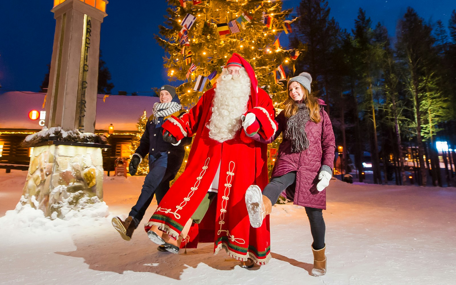 Santa Claus with visitors at Santa’s Village under a lit Christmas tree.