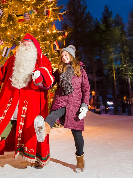 Santa Claus with visitors at Santa’s Village under a lit Christmas tree.