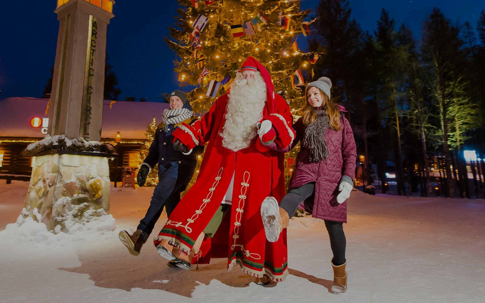 Santa Claus with visitors at Santa’s Village under a lit Christmas tree.