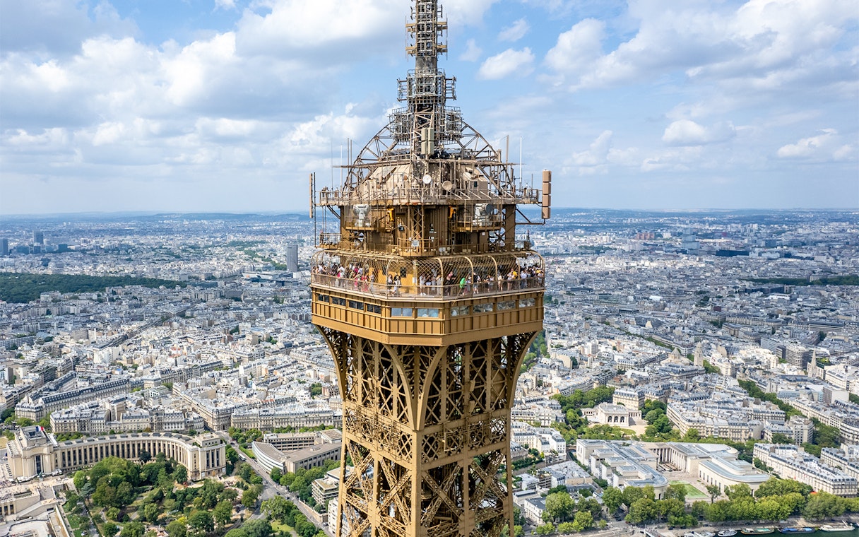 Eiffel Tower summit with Paris cityscape in the background.