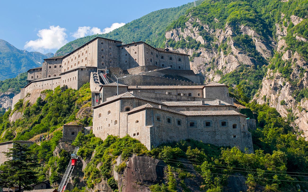 Guided tour of the Fortress of Bard in Italy, nestled in a mountainous landscape.