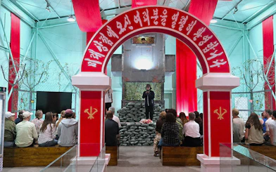 Visitors seated at North Korea Experience Center under red arch with Korean script.