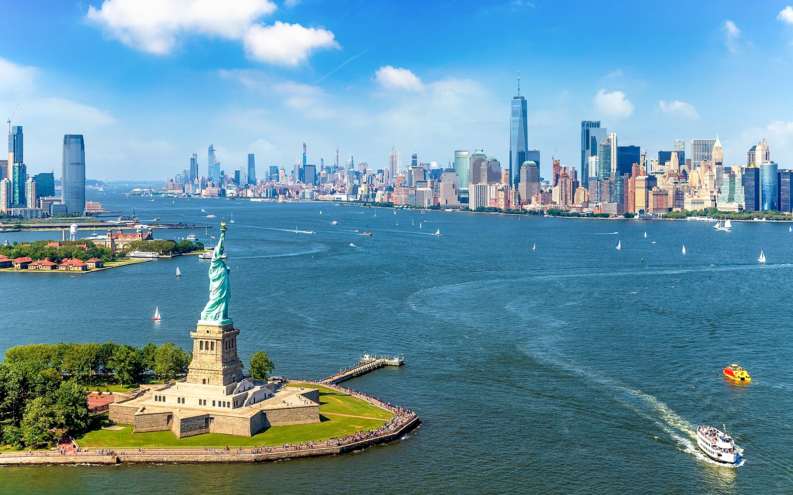 Statue of Liberty with New York City skyline and ferry in the harbor.