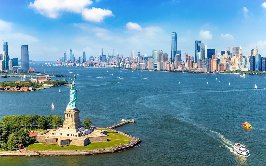 Statue of Liberty with New York City skyline and ferry in the harbor.