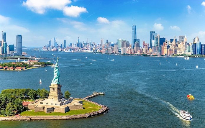 Statue of Liberty with New York City skyline and ferry in the harbor.