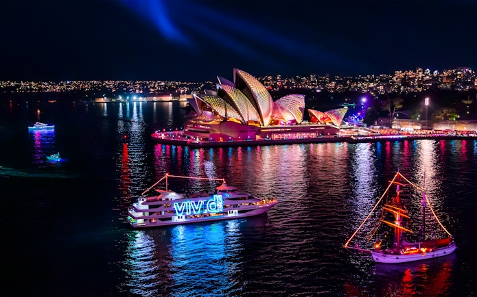 Boats illuminated in Sydney Harbour during Vivid Festival with Sydney Opera House in the background.