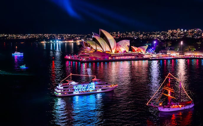 Boats illuminated in Sydney Harbour during Vivid Festival with Sydney Opera House in the background.