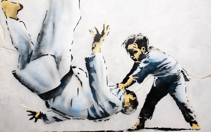 Street art of a child flipping an adult, featured in The World of Banksy exhibit, Lisbon.