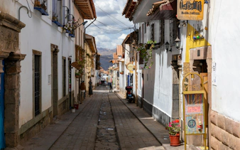 Narrow cobblestone street in San Blas, Cusco, Peru with colorful signs and colonial architecture.