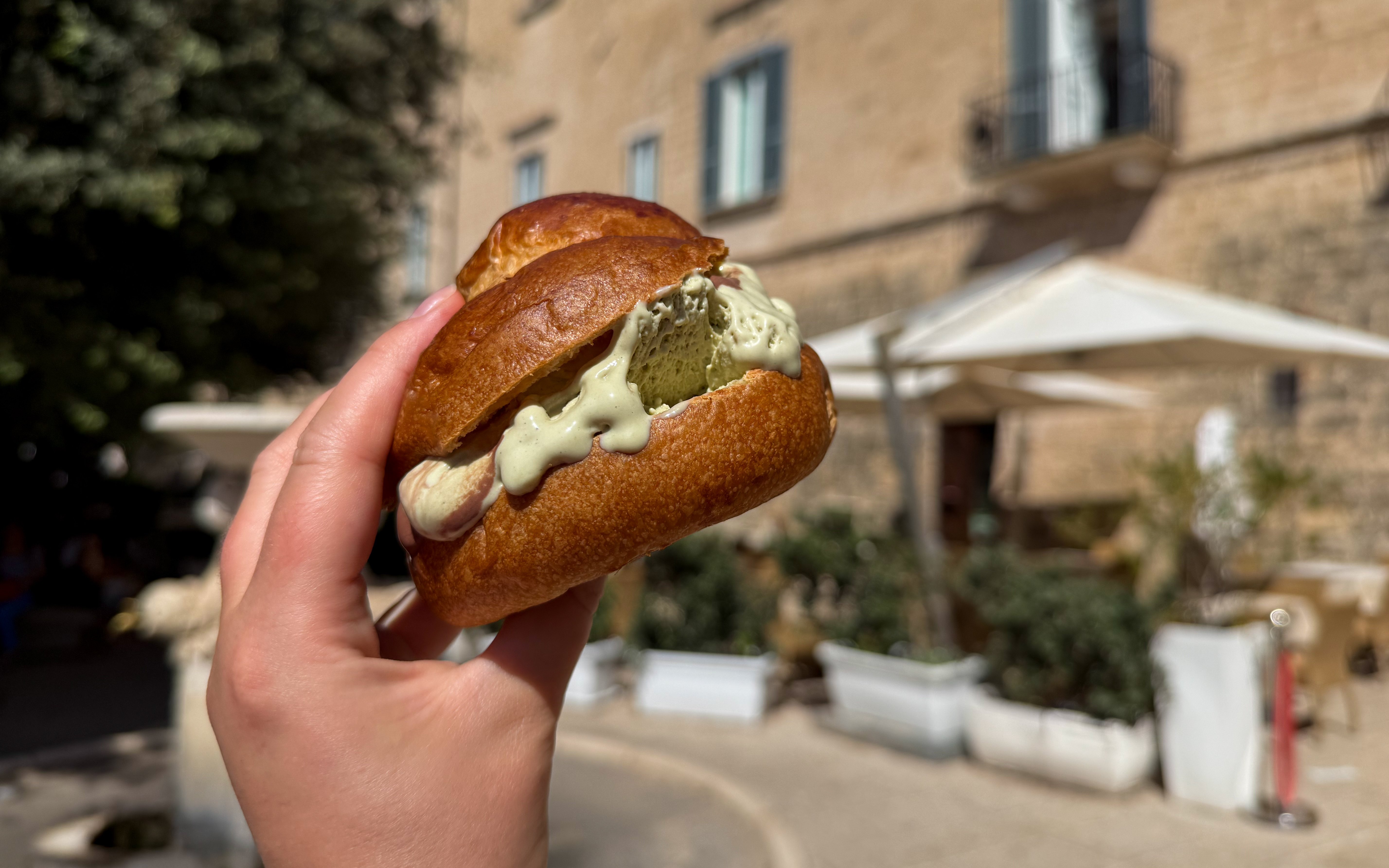 Traditional Sicilian brioche bun with pistachio gelato held in hand outdoors.