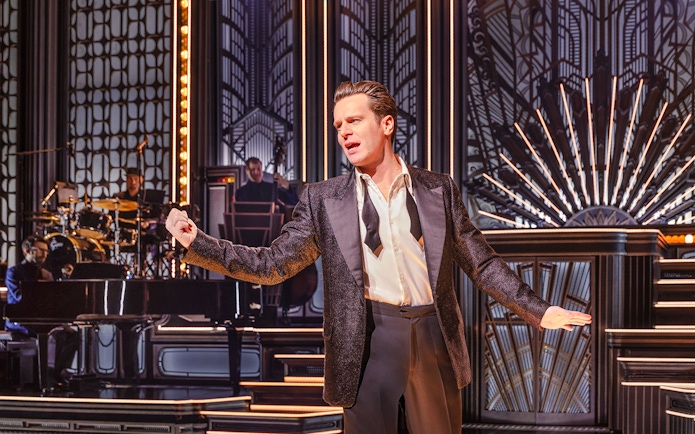 Performer on stage in a vintage-themed musical show with band in background.