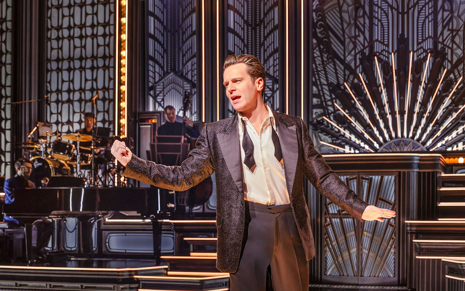 Performer on stage in a vintage-themed musical show with band in background.