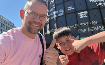 Father and son giving thumbs up in front of Berlin street art during city exploration game.