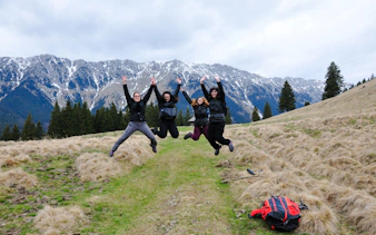 Group jumping on trail with Piatra Craiului mountains in background, Brasov trek.