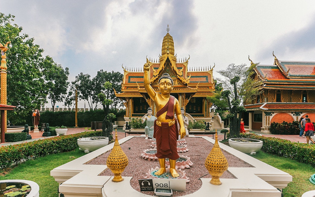 Golden Buddha statue at Erawan Museum with ornate temple in background, Ancient City tour.