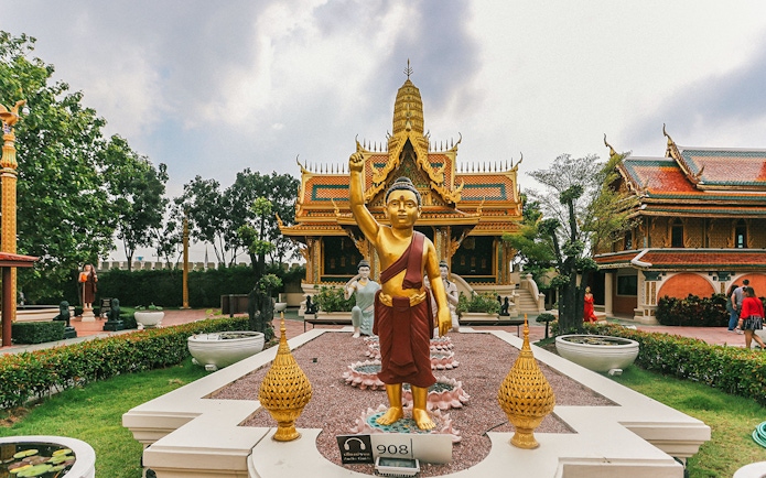 Golden Buddha statue at Erawan Museum with ornate temple in background, Ancient City tour.