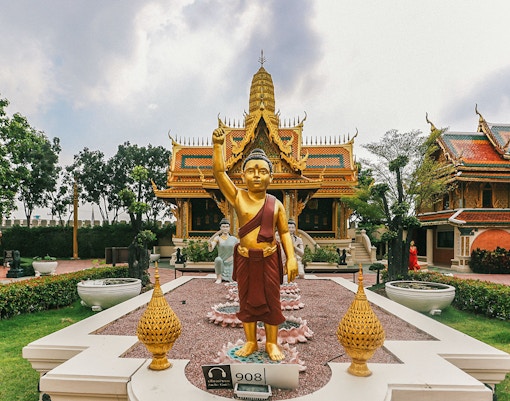 Golden Buddha statue at Erawan Museum with ornate temple in background, Ancient City tour.