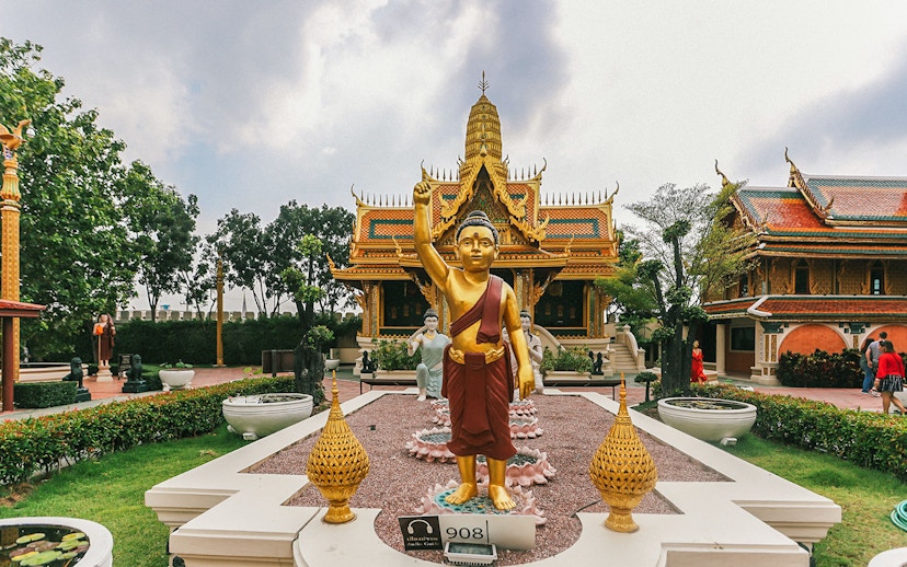 Golden Buddha statue at Erawan Museum with ornate temple in background, Ancient City tour.
