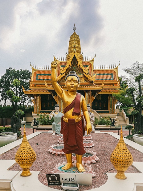 Golden Buddha statue at Erawan Museum with ornate temple in background, Ancient City tour.