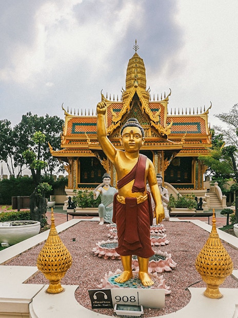 Golden Buddha statue at Erawan Museum with ornate temple in background, Ancient City tour.