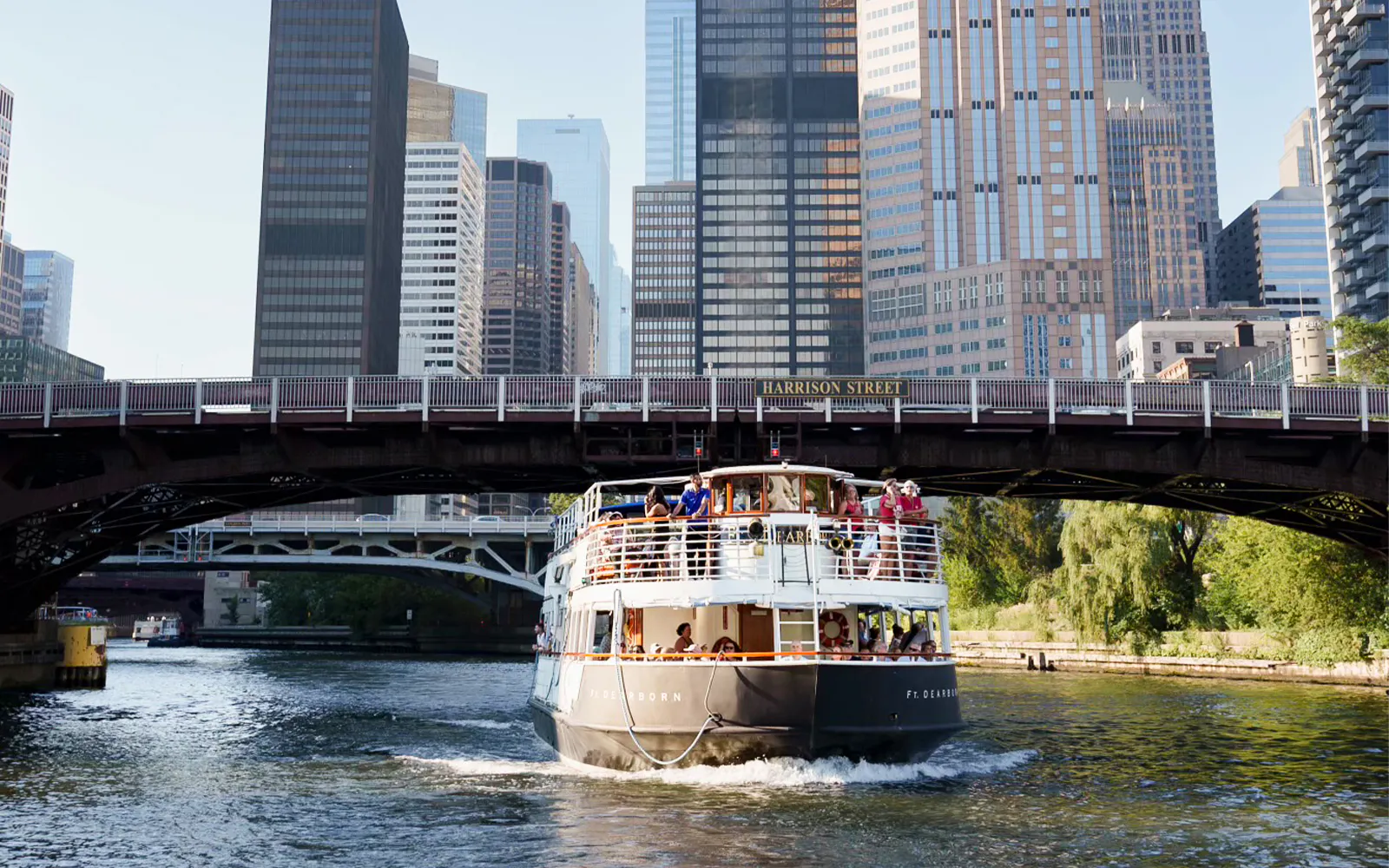 Cruise boat on Chicago River near skyscrapers and Harrison Street Bridge.