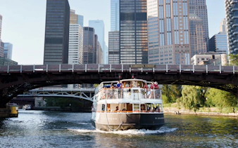 Cruise boat on Chicago River near skyscrapers and Harrison Street Bridge.