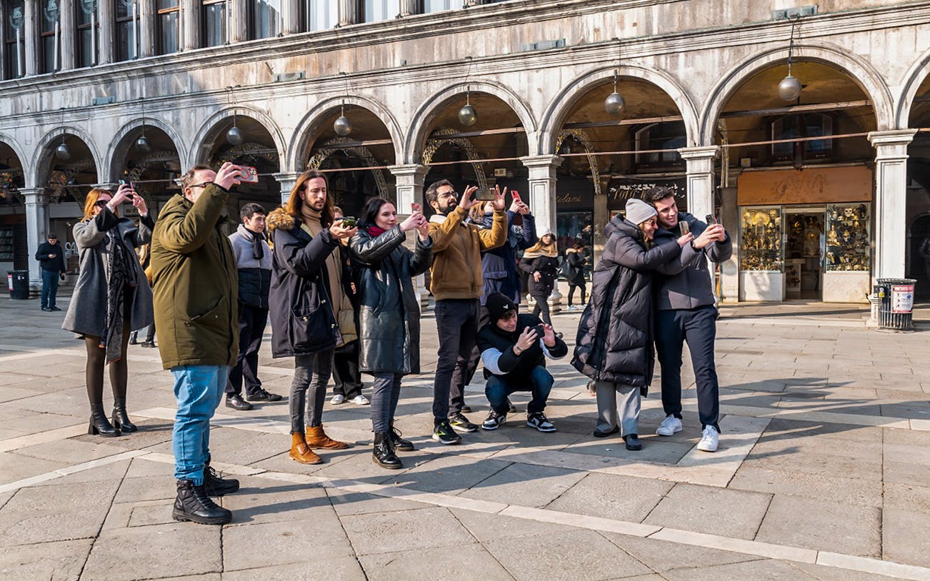 Group of tourists taking photos in St. Mark's Square during a walking tour in Venice.