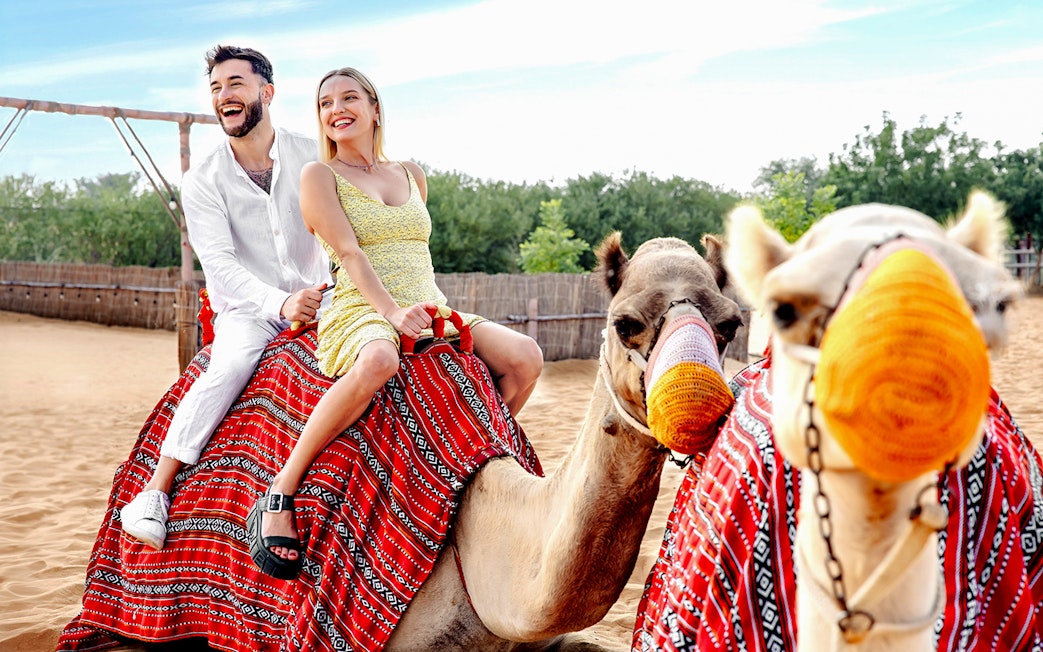 Couple riding camels in desert setting, part of hot air balloon tour with breakfast and quad biking.