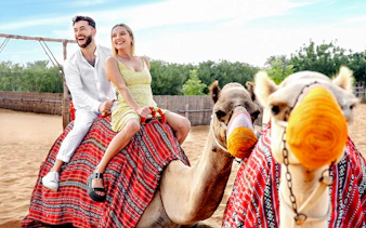 Couple riding camels in desert setting, part of hot air balloon tour with breakfast and quad biking.