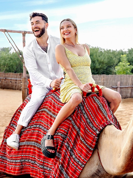 Couple riding camels in desert setting, part of hot air balloon tour with breakfast and quad biking.