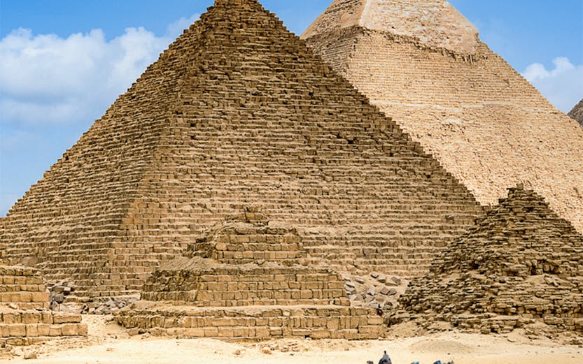 Pyramids of Giza with camels in the foreground under a clear blue sky.