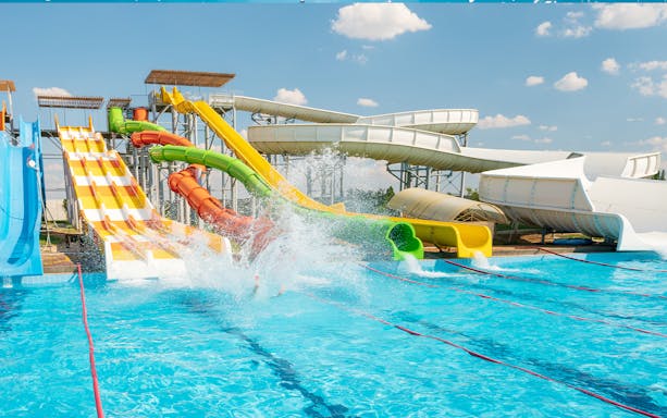 Water slides at Aqualand with splashes in the pool, showcasing vibrant slides and fun activities.